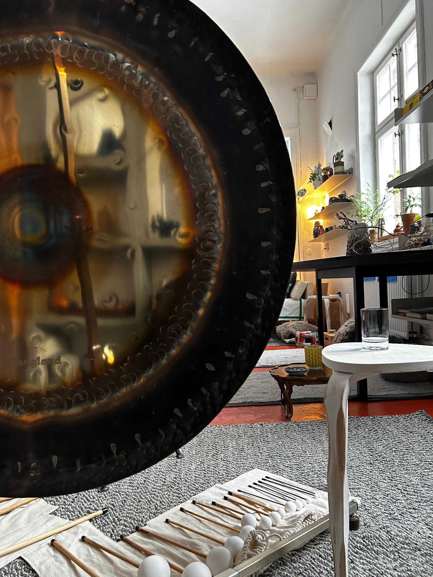 Bronze gong backlit by studio window with mallets on the floor